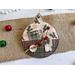 ornament with holly background, includes buttons, cranberry pips, a stamp, mini ticket strip, and a mini ornament tag.